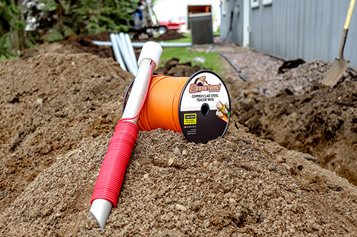 Ground rod laying against orange tracer wire in the dirt