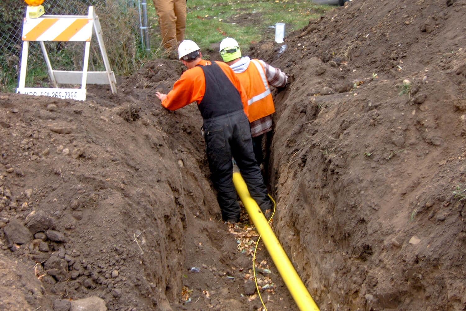 Two men in orange putting a yellow pipe in the ground