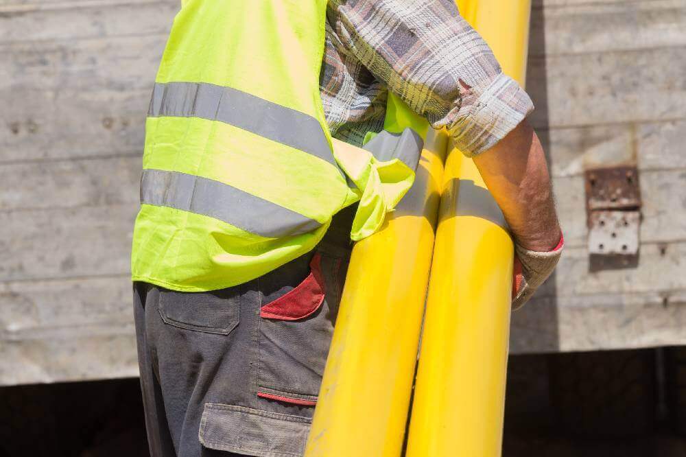 Man in reflective vest carrying two yellow pipes