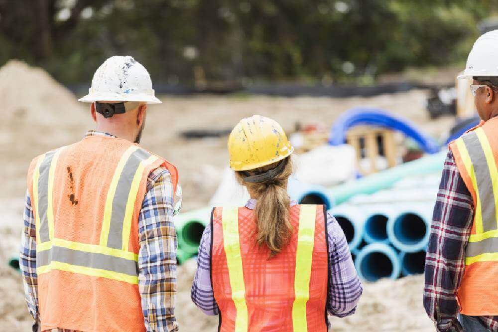 Three construction workers looking at a worksite with pipes